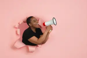 Mulher segurando megafone em fundo rosa Uma mulher animada segura um megafone enquanto emerge de um fundo rosa rasgado, representando comunicação, marketing, empoderamento ou uma mensagem impactante.