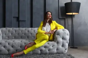 Mulher rica vestindo um elegante terninho amarelo e sapatos vermelhos, sentada em um sofá de luxo em um ambiente sofisticado. Representação do empoderamento feminino e sucesso financeiro.